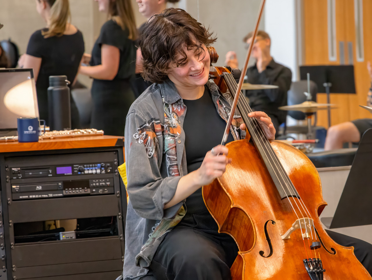 Hannah Paulus smiling while playing cello in a rehearsal room